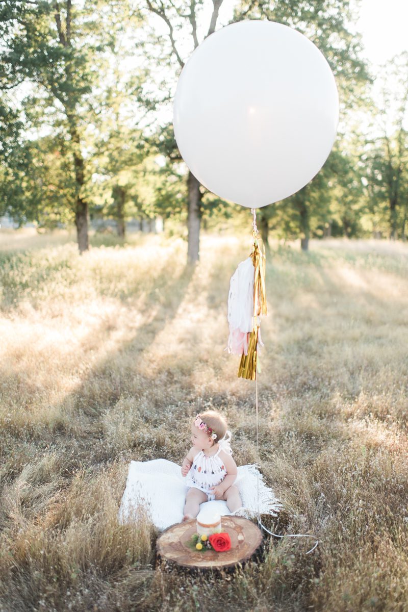 A baby girl celebrating her first birthday, with a flower crown and a balloon.